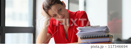 Overworked woman sitting at table littered with papers Overworked woman sitting at table littered with papers 117346694