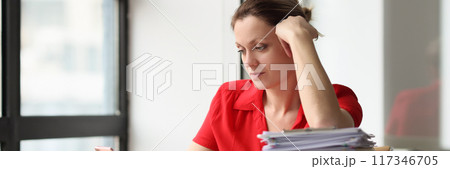 Woman sitting at desk littered with papers Woman sitting at desk littered with papers 117346705