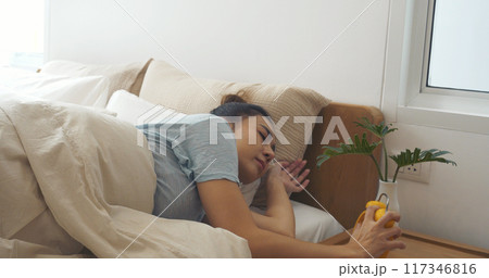 Asian women sleep wake up in white cozy bedroom happy time morning sunrise. Beautiful chinese use hand stop time alarm clock. Happy person lifestyle wake up in morning wellbeing relax sleepy napping 117346816