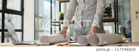 Designer standing near work desk with rolls of paper 117346820