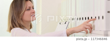 Female doctor pick up folder from row in medical clinic Female doctor pick up folder from row in medical clinic 117346846