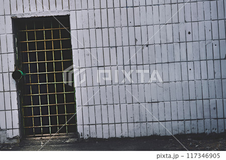 Grunge metal door hole with bars on old white tiled wall Grunge metal door hole with bars on old white tiled wall 117346905