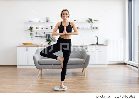 Woman practicing yoga at home in tree pose in living room 117346963