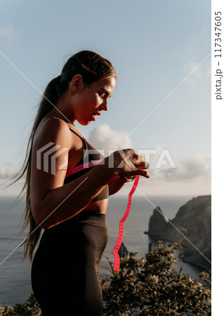 A woman is holding a pink tape measure and is measuring her breasts after morning fitness 117347605