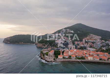 Old medieval town stone houses with red roofs and church bell towers. Budva is the center of tourism in Montenegro and a summer vacation destination. Aerial drone cityscape in Montenegro. Old medieval town stone houses with red roofs and church bell towers. Budva is the center of tourism in Montenegro and a summer vacation destination. Aerial drone cityscape in Montenegro. 117348715