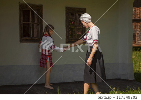 A woman and a little girl hold hands happily in front of a house 117349202