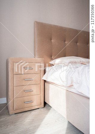 Beige dresser with four drawers near the bed. Well organized bedroom in natural light. 117350366