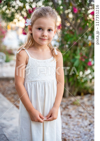 Portrait of little girl in white dress happy smiling on blooming park background in Croatia 117351216