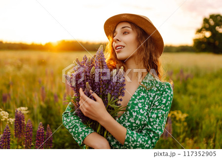 A beautiful woman with a bouquet of lupins, collects flowers, inhales fresh floral air. A beautiful woman with a bouquet of lupins, collects flowers, inhales fresh floral air. 117352905