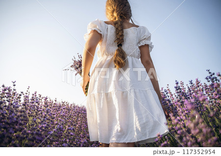 Lavender field girl. Back view happy girl in white dress with a scythe runs through a lilac field of lavender. Aromatherapy travel 117352954