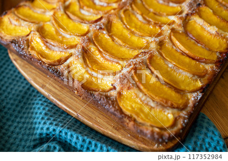 A dessert made of sliced peaches is on a wooden cutting board. The dessert is covered in sugar and looks delicious. 117352984