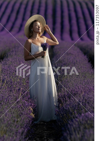 A woman in a white dress stands in a field of purple flowers A woman in a white dress stands in a field of purple flowers 117353097