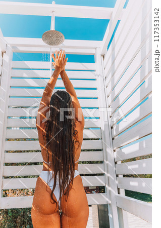 A woman in a bikini stands in front of a white shower stall. She is smiling and she is enjoying the moment A woman in a bikini stands in front of a white shower stall. She is smiling and she is enjoying the moment 117353142