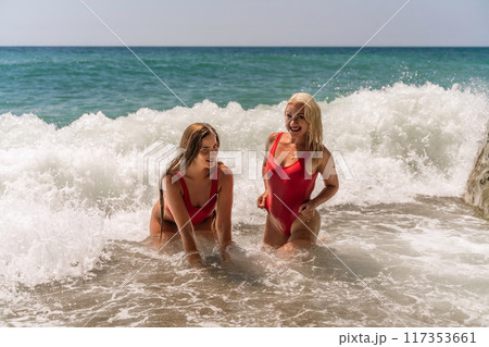 Women ocean play. Seaside, beach daytime, enjoying beach fun. Two women in red swimsuits enjoying themselves in the ocean waves. Women ocean play. Seaside, beach daytime, enjoying beach fun. Two women in red swimsuits enjoying themselves in the ocean waves. 117353661