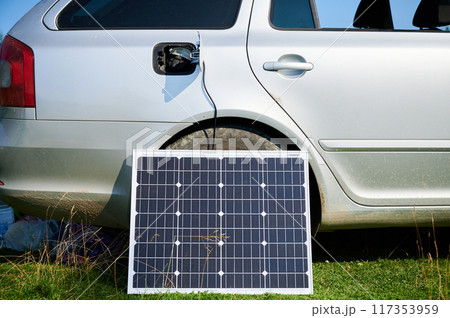 Solar panel connected via charging cable to car's charging port. Transition from internal combustion engines to electric cars, Renewable energy sources and sustainable transportation solutions. 117353959