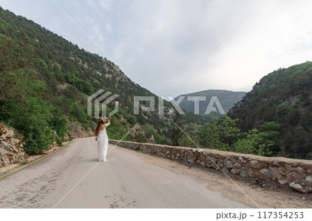 A woman is walking down a road in the mountains 117354253