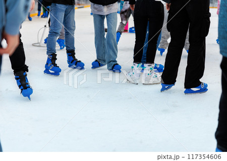 Close-up bottom people group wearing ice skates on outdoor ice skating rink city market park square. Christmas winter seasonal social and recreational atmosphere of holidays family outside activities 117354606