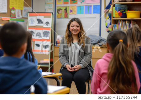 Cheerful young teacher sitting and interacting with her attentive elementary school class 117355244