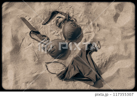 A black bikini is resting on warm sand under the sun A black bikini is resting on warm sand under the sun 117355307