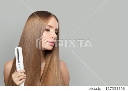 Lovely fashion model woman using hair straighteners iron on white background.  117355596