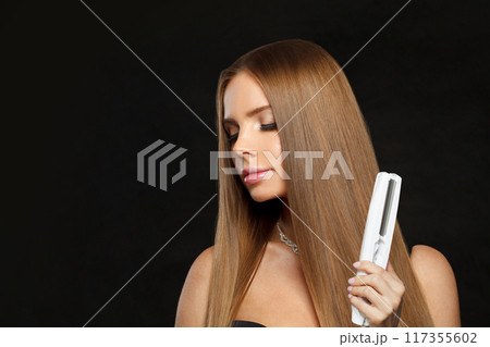 Fashion portrait of woman with hair straightener iron in studio isolated on black background. Fashion portrait of woman with hair straightener iron in studio isolated on black background. 117355602