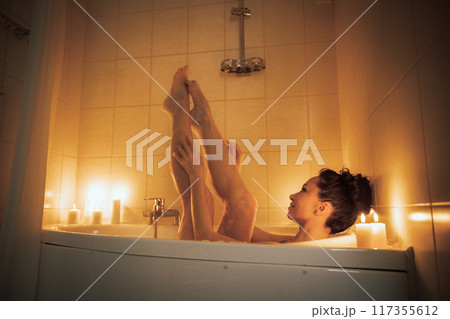 A woman is in a bathtub with candles lit around her. She is barefoot and has her legs up in the air. A woman is in a bathtub with candles lit around her. She is barefoot and has her legs up in the air. 117355612