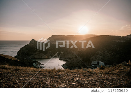 Two young girls are standing on a hillside, one of them wearing a white dress. The sun is shining brightly, creating a warm and inviting atmosphere. The girls seem to be enjoying their time together. 117355620