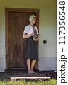 A Traditional Woman dressed in a colorful Folk Costume stands gracefully by a Wooden Door 117356548