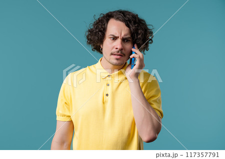 Irritated handsome man talking on mobile phone. Guy in stress, Blue studio. Irritated handsome man talking on mobile phone. Guy in stress, Blue studio. 117357791