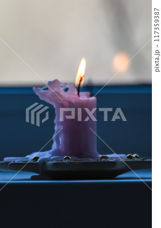 Burning pink candle in a glass holder on the windowsill. 117359387