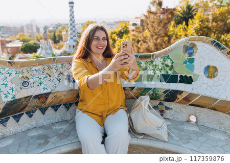 Beautiful 30s female in Gaudi garden, Spain, Barcelona. Young traveling woman taking selfie outdoors. Concept of travel, tourism and vacation in city. High quality photo Beautiful 30s female in Gaudi garden, Spain, Barcelona. Young traveling woman taking selfie outdoors. Concept of travel, tourism and vacation in city. High quality photo 117359876