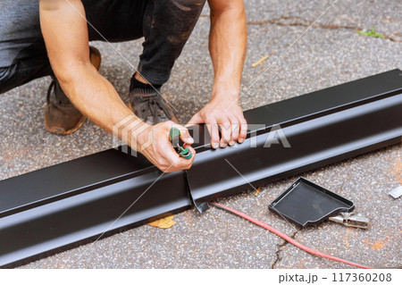 An aluminum rain gutter is bent using machine tool then cut to the required dimensions with shears 117360208