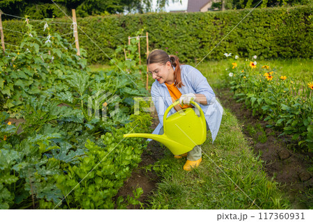 Happy woman taking care of flowers outdoors in garden, watering with can. Female preparing for preparing flowers for international women day. High quality photo Happy woman taking care of flowers outdoors in garden, watering with can. Female preparing for preparing flowers for international women day. High quality photo 117360931