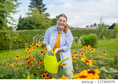 Happy woman taking care of flowers outdoors in garden, watering with can. Female preparing for preparing flowers for international women day. High quality photo Happy woman taking care of flowers outdoors in garden, watering with can. Female preparing for preparing flowers for international women day. High quality photo 117360976