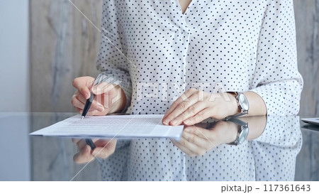 Businesswoman analyzing document at desk. Close-up of a professional auditor or lawyer reviewing a lengthy paper report in office setting. Business people concept 117361643