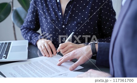Detailed view of two business people or lawyers signing a contract with a laptop nearby Detailed view of two business people or lawyers signing a contract with a laptop nearby 117361700