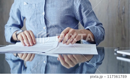 Businessperson analyzing document at desk. Close-up of a professional auditor or lawyer reviewing a lengthy paper report in office setting. Business people concept Businessperson analyzing document at desk. Close-up of a professional auditor or lawyer reviewing a lengthy paper report in office setting. Business people concept 117361789