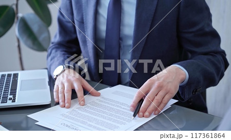 Businessman signing contract at desk. Close-up of a male executive's hands signing a legal document in a modern office setting 117361864