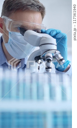 Man scientist with protective glasses, mask and gloves is using microscope in laboratory, vertical portrait of researcher. Microbiology and science 117361940