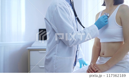 Doctor and patient. Physician wearing blue medical gloves is using stethoscope examining woman lungs in clinic. Medicine concept 117362189