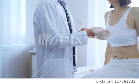 Doctor and patient. Physician putting white medical gloves is ready to examine female patient in clinic. Orthopedics and medicine Doctor and patient. Physician putting white medical gloves is ready to examine female patient in clinic. Orthopedics and medicine 117362232