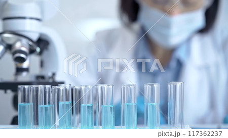 Test tubes with a blurred scientist in a lab coat in the background 117362237