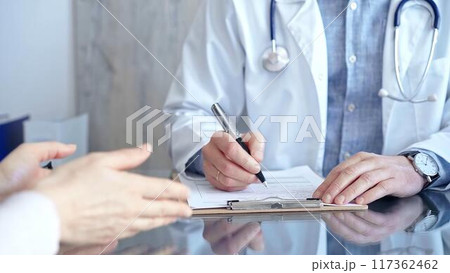 Doctor and patient conversation with clipboard in clinic office. Physician is making notes while listening woman. Medicine and Health care 117362462