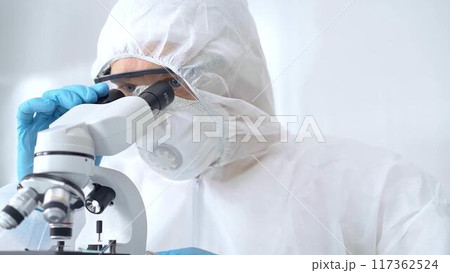 Scientist is analyzing samples using a microscope in a laboratory setting. Close-up of a focused researcher in a protective gear. Science concept Scientist is analyzing samples using a microscope in a laboratory setting. Close-up of a focused researcher in a protective gear. Science concept 117362524