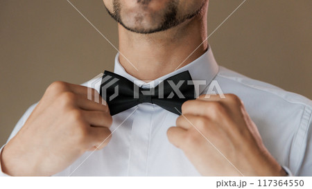 Groom adjusting his black bow tie, symbolizing elegance and style on his wedding day Groom adjusting his black bow tie, symbolizing elegance and style on his wedding day 117364550