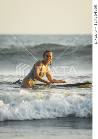 Young woman in swimsuit smiling while surfing on the beach 117364869