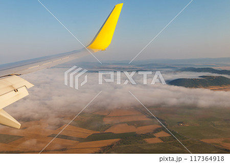 Wing of airplane flying above the clouds in the blue sky 117364918
