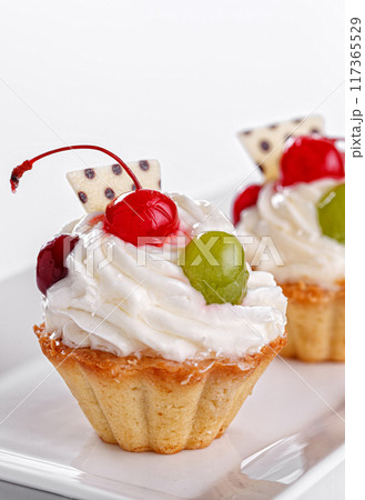 Beautiful cream cakes with cherries and grapes on a plate on a white background Beautiful cream cakes with cherries and grapes on a plate on a white background 117365529