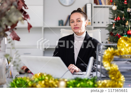 Portrait of successful business woman with New Years tinsel and Christmas tree in office 117365681