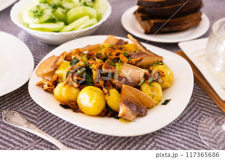 Baked potatoes with chanterelles and bacon served with herbs and lightly salted cucumbers on table 117365686